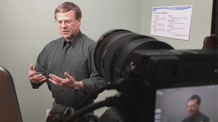 Man gesturing and explaining something in front of a camera.