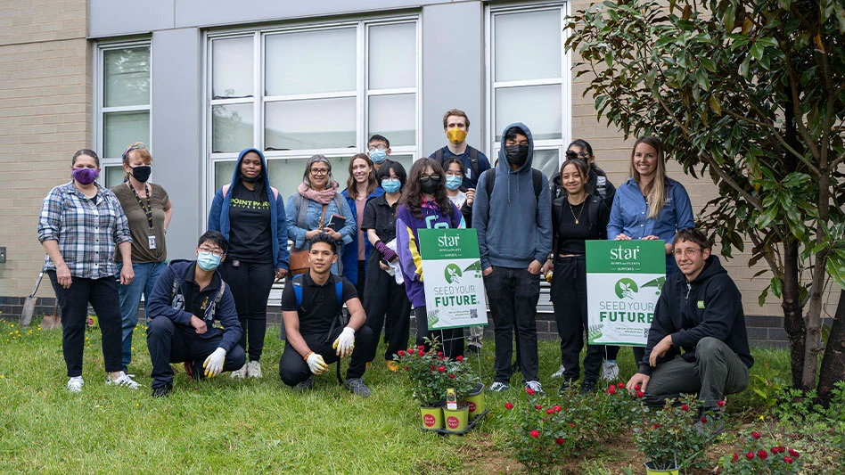 A group of individuals gather on the lawn in front of a building around flowers