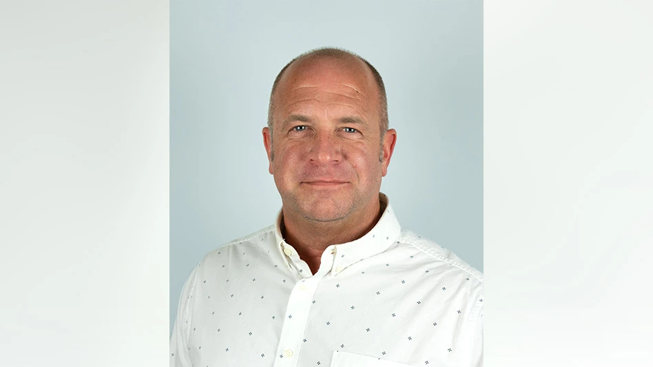 A man wearing a white button-up dress shirt with small dark blue flowers poses for a headshot photo.