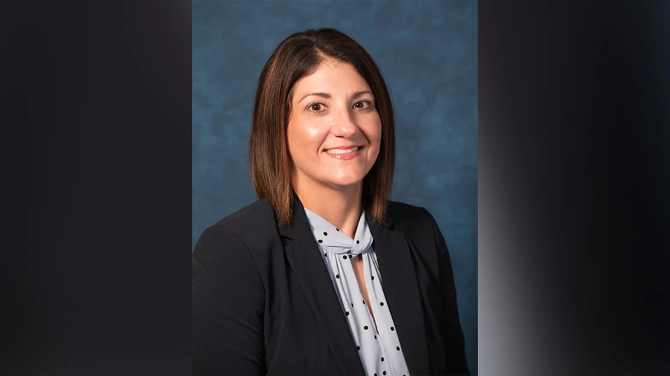 A smiling woman with shoulder length brown hair wearing a black suit jacket and white shirt with black polka dots. She is visible from the chest up in this headshot photo in front of a blue background.