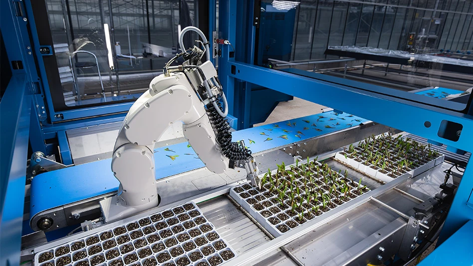 A white robotic arm in a blue machine hovers over trays of small green seedlings in brown soil.