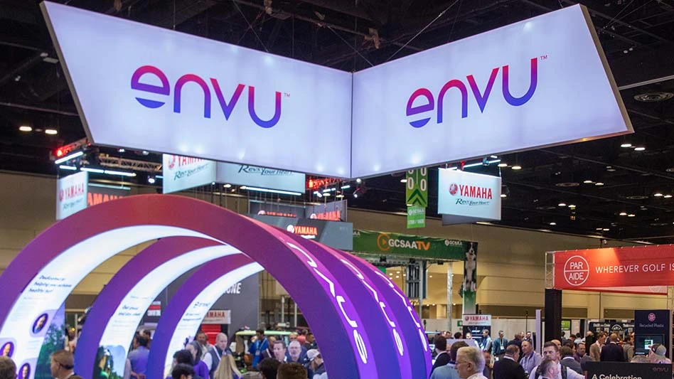 Two large white signs hang from the ceiling of a convention center. There's a logo on each that reads envu TM in gradient red, purple and blue letters. Three purple arches are underneath, and a crowd of people is also pictured.