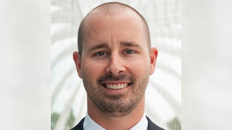 A smiling man with short dark hair and beard in a white dress shirt and dark suit jacket.