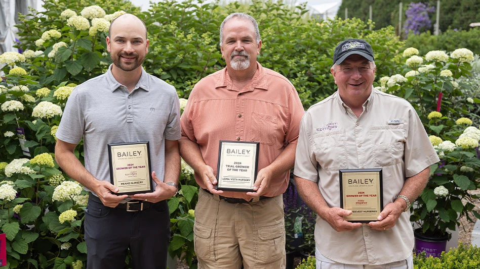 Three men stand in front of hydrangea bushes as they hold gold plaques.
