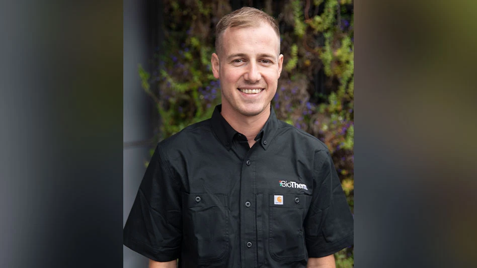 A smiling man with short blonde hair in a black short-sleeve button-up shirt that reads BioTherm above the chest pocket.