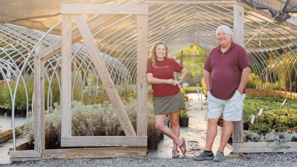 A father and daughter stand outside a greenhouse.