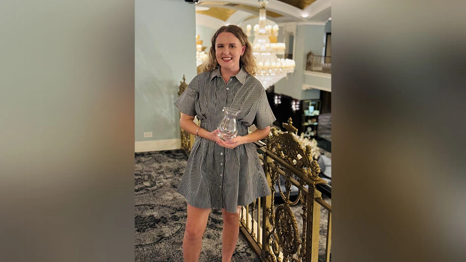 A women with blonde, curly hair holds a clear, glass award in a ballroom with chandeliers.