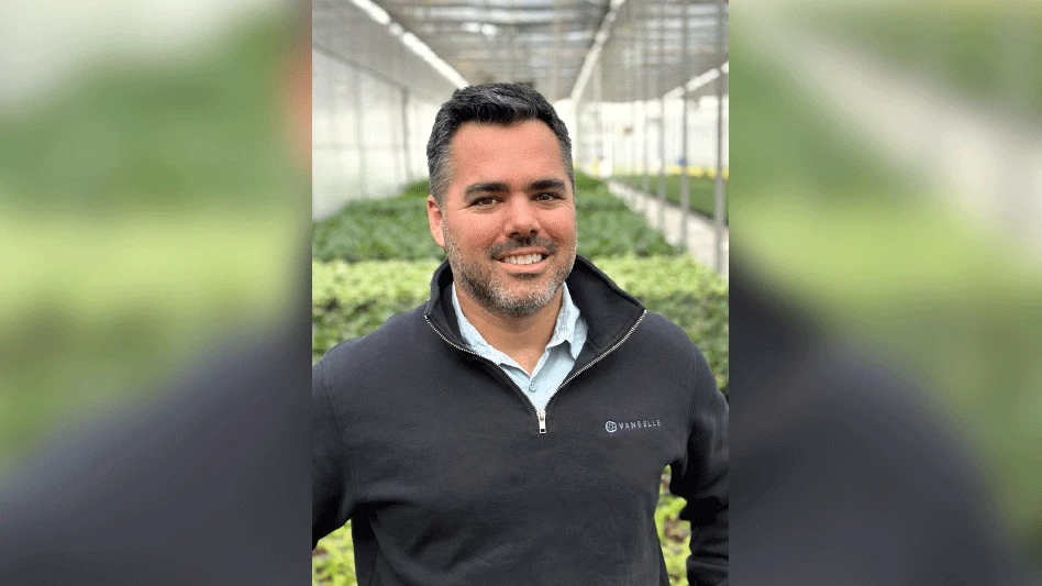 A man with short black hair standing inside a greenhouse.