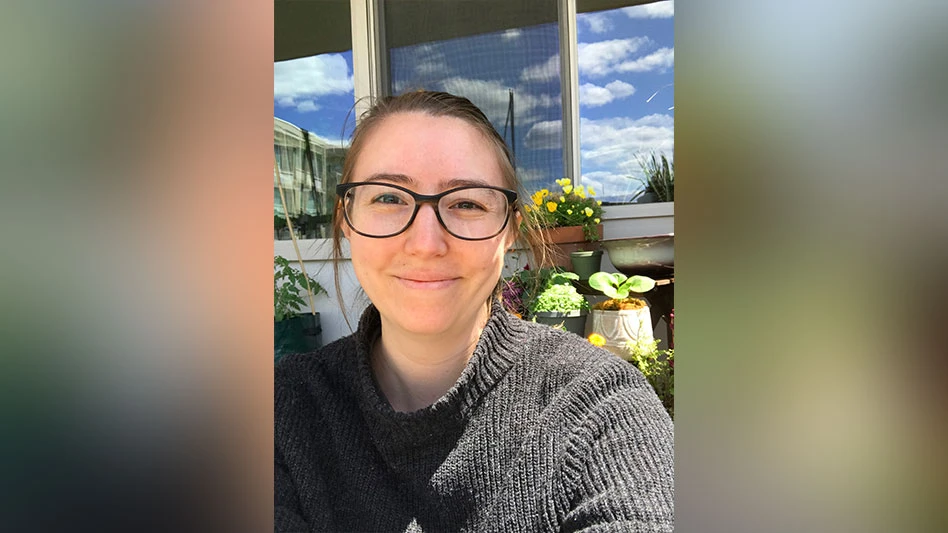 A woman with brown hair wearing a black sweater softly smiles in a selfie photo.