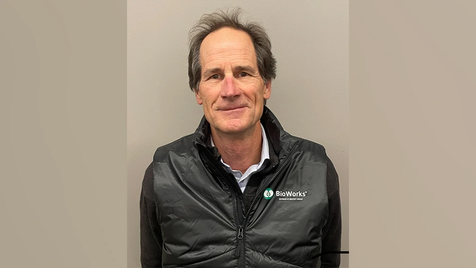 A smiling man with short black hair wearing a black shirt and vest that reads BioWorks in white letters on the chest. He stands in front of a beige background.