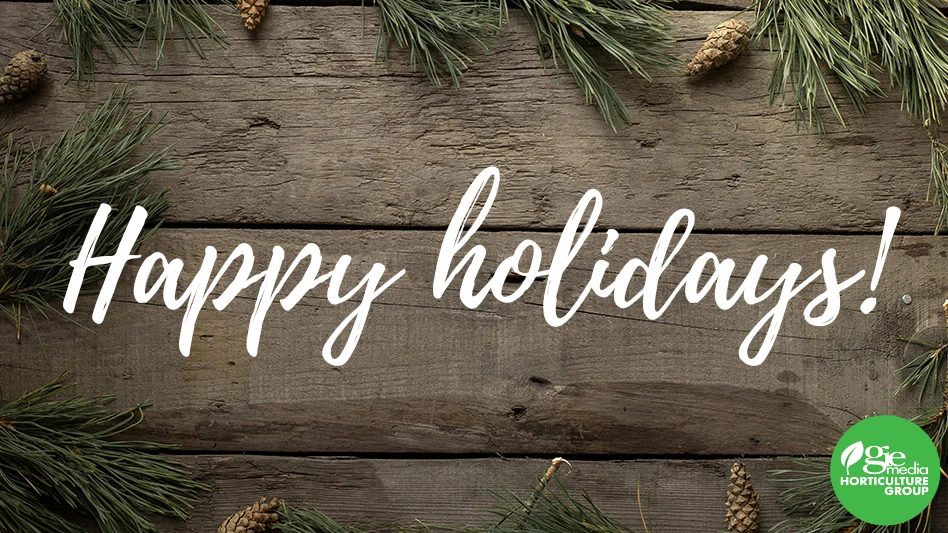 A graphic with a brown wooden background with greenery and pinecones around the edges, with white cursive letters in the middle reading Happy holidays! In the bottom right is a circular logo with a green background and white text reading GIE Media Horticulture Group.