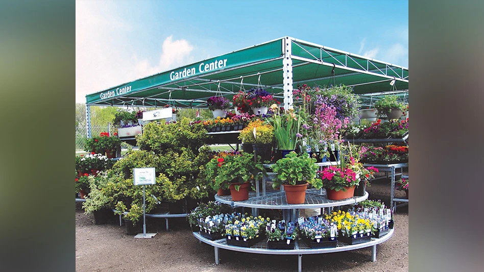 An outdoor garden center, with tables full of potted plants and flowers and a green shade covering with white text reading Garden Center.