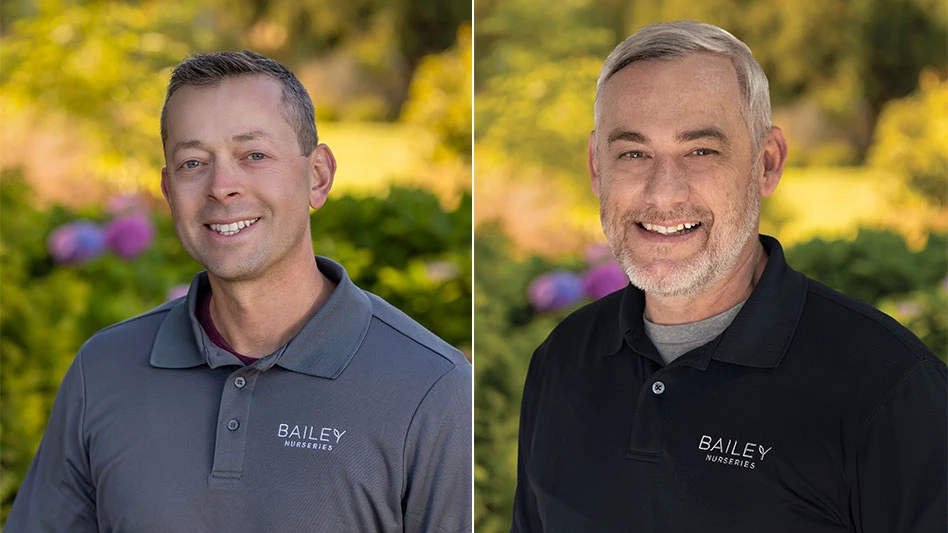 Two middle-aged men wearing black/gray polos in front of a blurred nature landscape background.