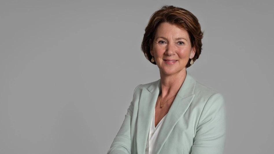 A smiling woman with short brown hair wearing a mint green blazer and white top visible from the waist up against a gray background.