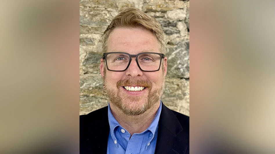 A headshot of a blonde middle-aged man. He has a short beard and black glasses. He's wearing a blue button-up shirt with a navy suit jacket.
