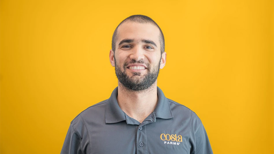 A smiling man in a gray polo shirt poses for a headshot photo in front of a yellow background.