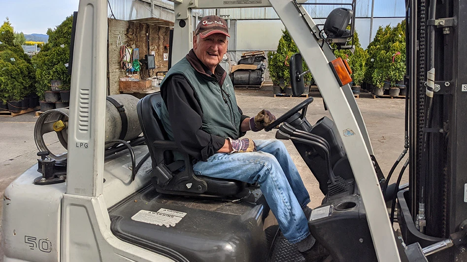 A smiling man sitting on a piece of farm equipment.