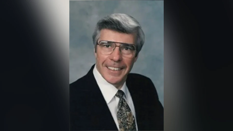 A smiling man with short gray wearing glasses, a white dress shirt, a tie and a black suit jacket.