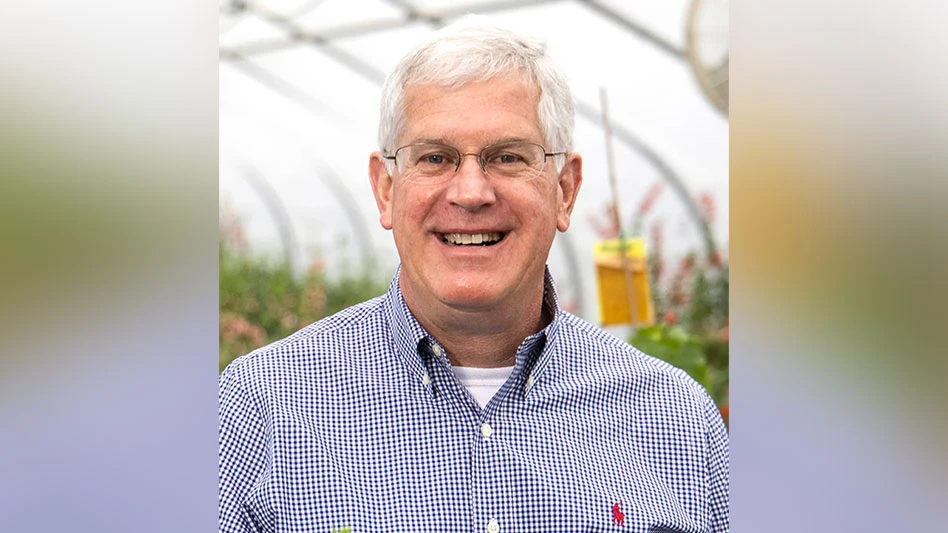 A headshot of man standing inside a greenhouse.