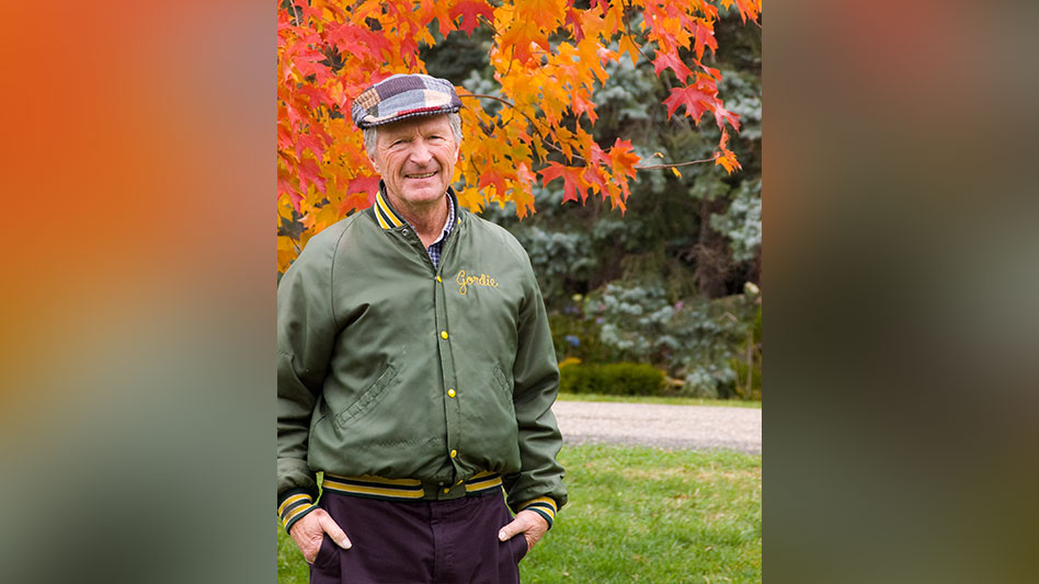 A smiling man standing outside in front of an orange and red maple tree.