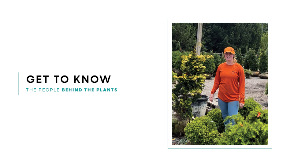 A women standing in a wholesale nursery surrounded by plants. She's wearing an orange t-short and hat.
