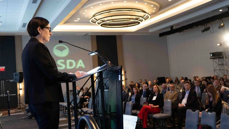 A woman stands at a podium in a room full of people for a conference.