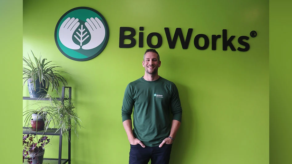 man in green shirt stands in front of a green wall with bioworks logo behind him