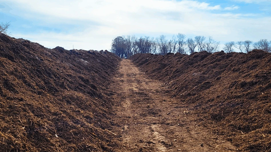 A brown compost pile with a path down the middle under a blue sky.