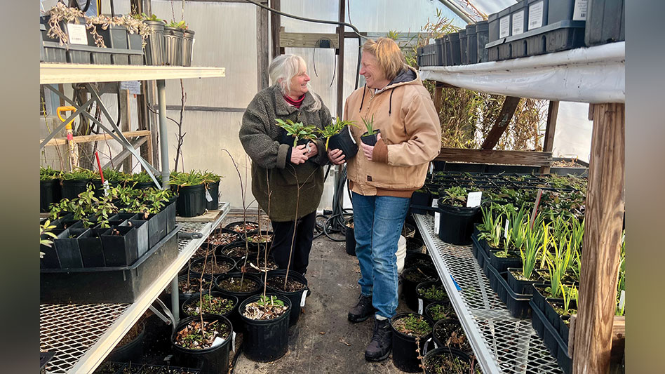 Two women stand inside a hoop house at a nursery.