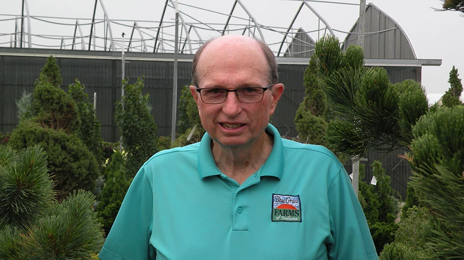 man in green shirt stands in front of shrubs
